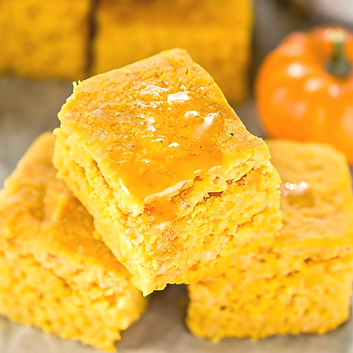 A stack of square pumpkin cornbread slices drizzled with sweet honey, perfect to pair with crockpot thanksgiving sides