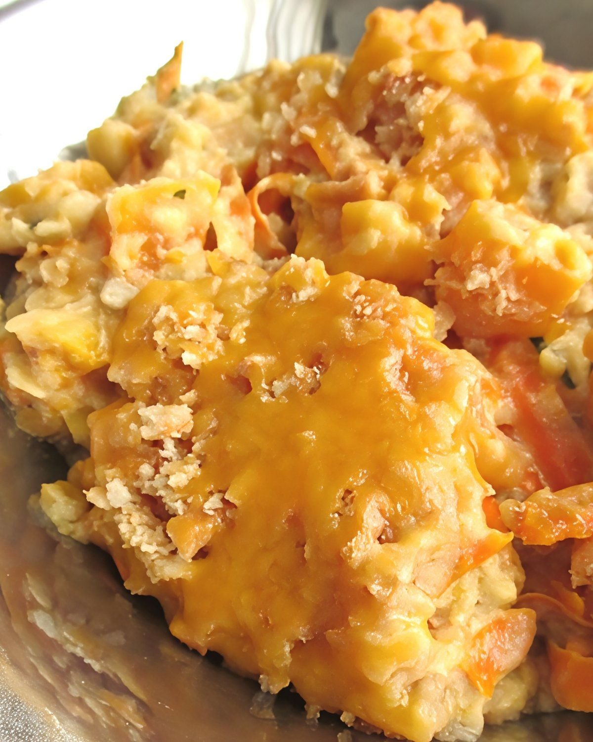 A silver serving bowl filled with cheesy slow-cooked squash casserole topped with a crispy cracker crust, featured as one of the best crockpot thanksgiving sides