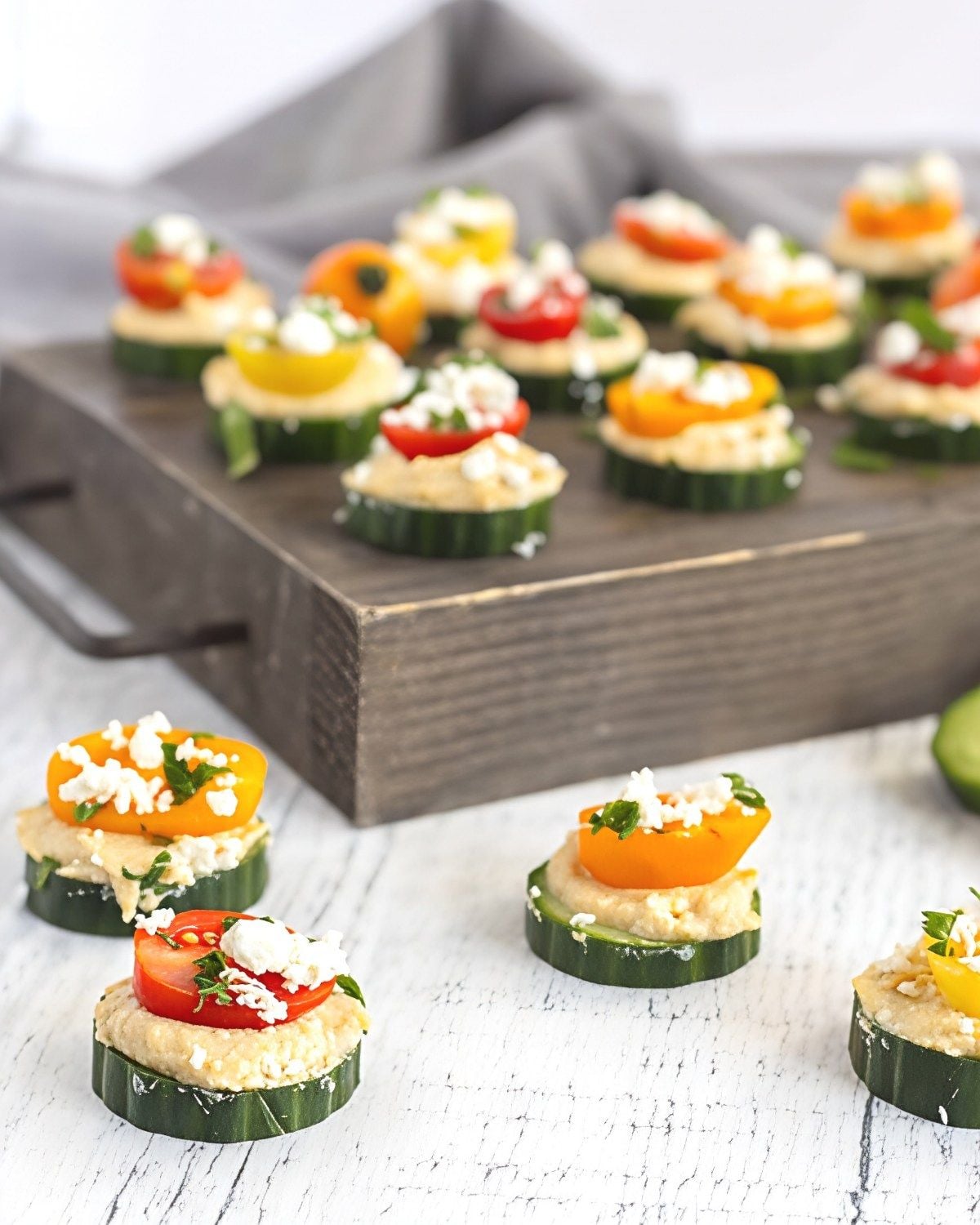 Fresh cucumber slices topped with smooth hummus, cherry tomatoes, and crumbled feta cheese served on a wooden tray for a healthy, light Thanksgiving appetizer.