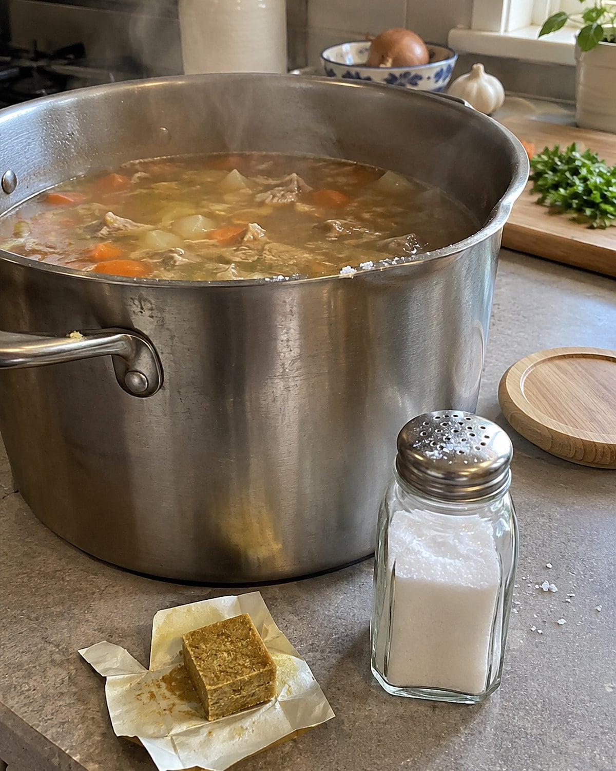 A bouillon cube and a salt shaker sit beside an open stockpot on the counter.