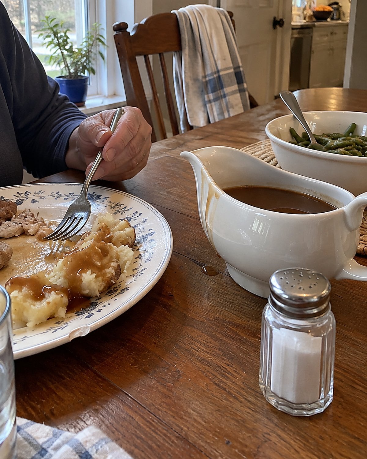 A gravy boat and salt shaker sit beside a half-finished plate of potatoes on a family dining table.