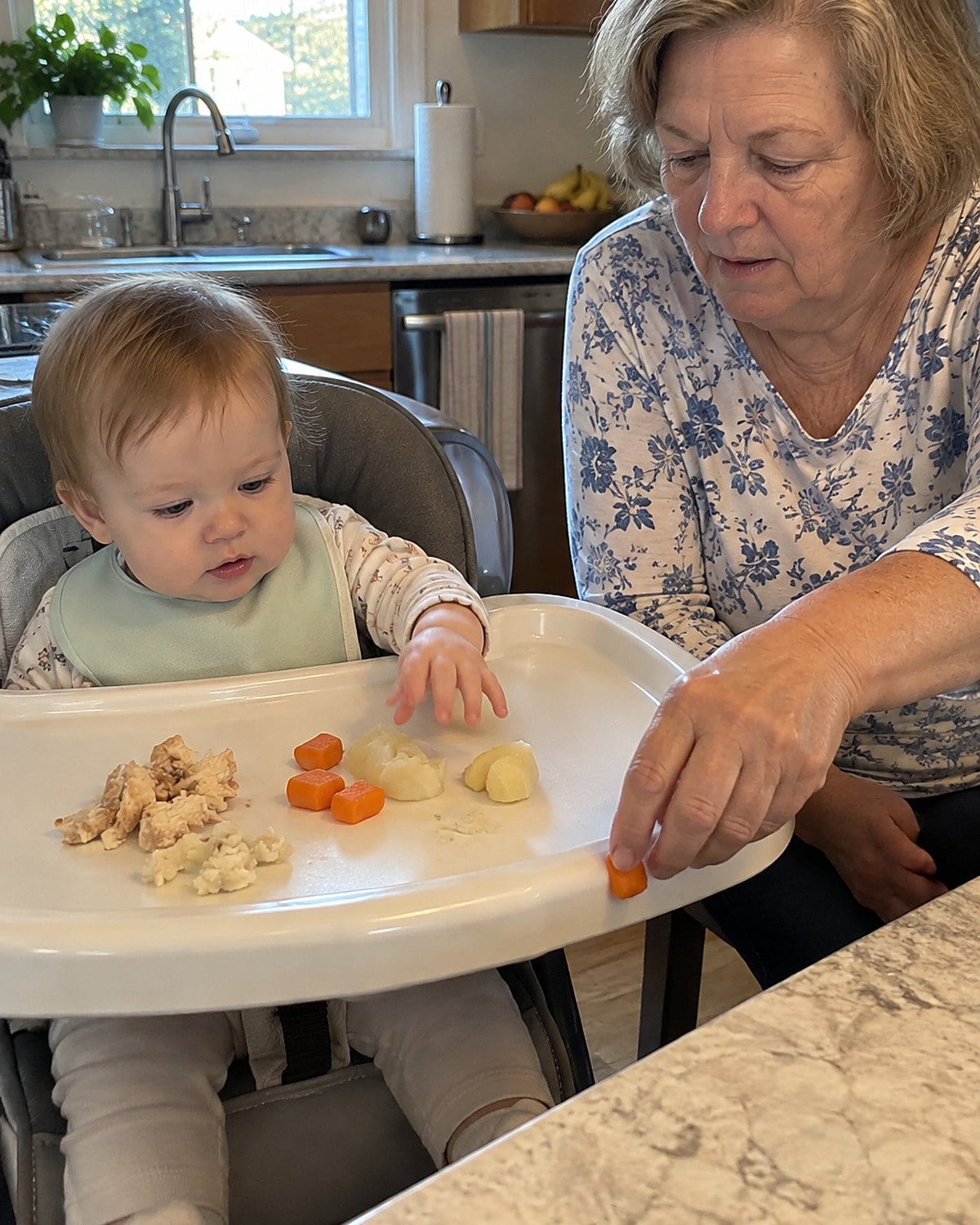 A child's hands reach across a high-chair tray with small servings of chicken, carrots, and potatoes.