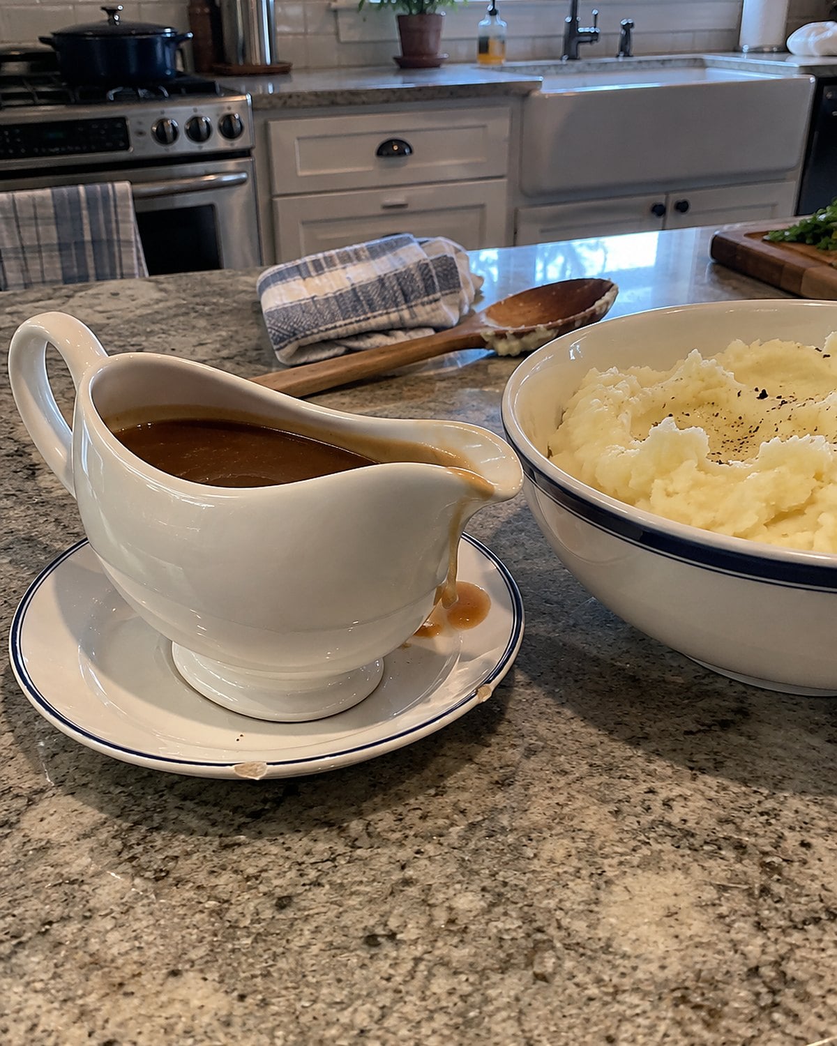 A gravy boat on a small saucer beside a bowl of mashed potatoes.