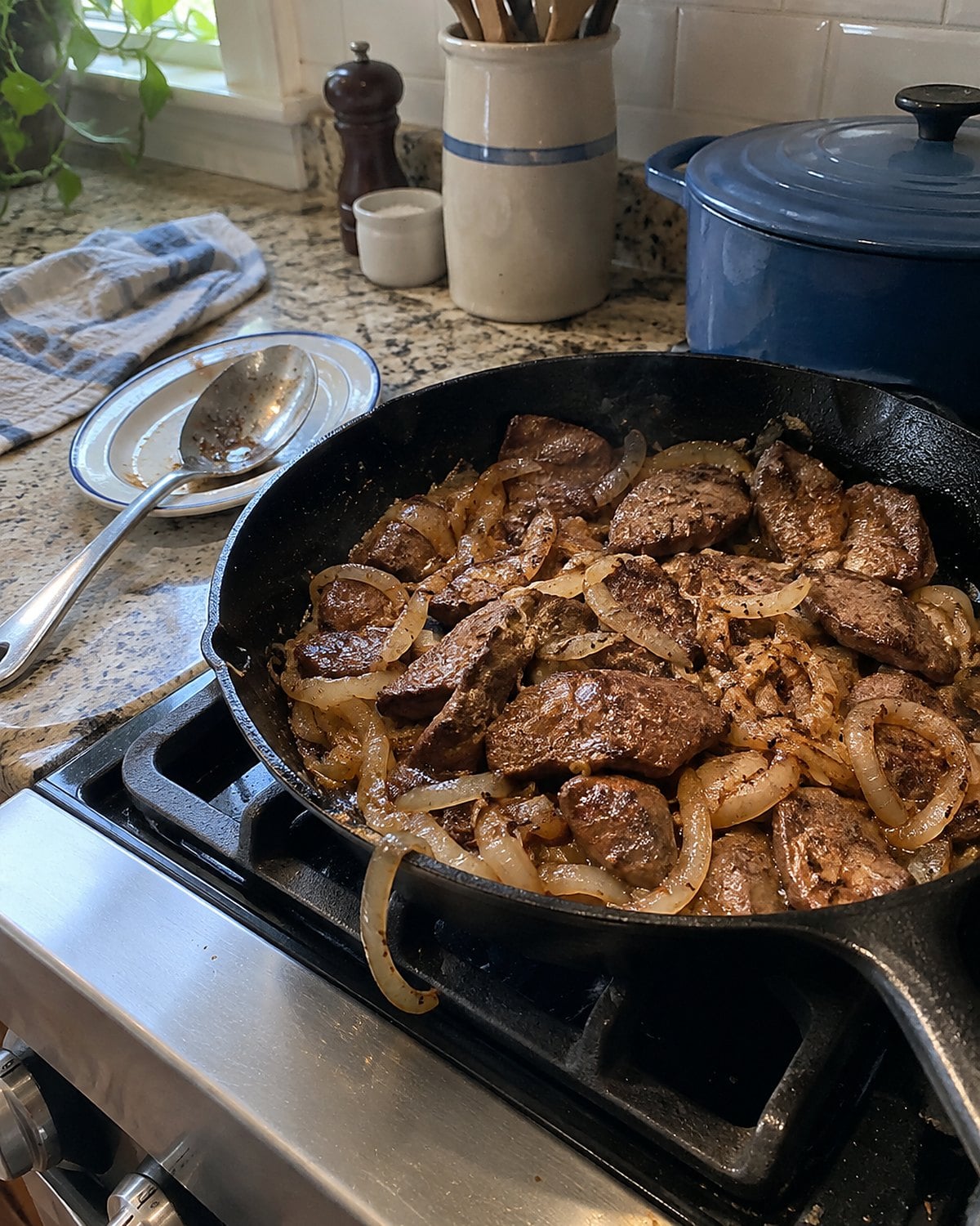 Liver and browned onions in a skillet on a stove, with a serving spoon resting nearby.