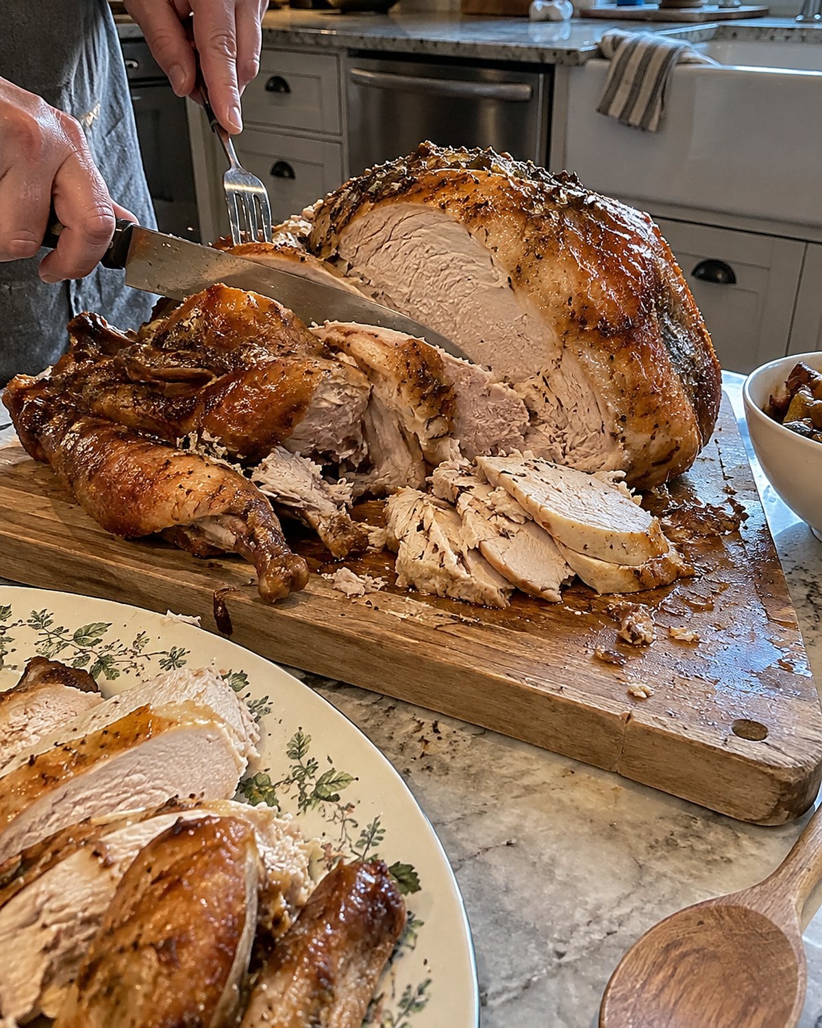 A partly carved roast turkey on a worn cutting board beside a serving platter on a kitchen counter.