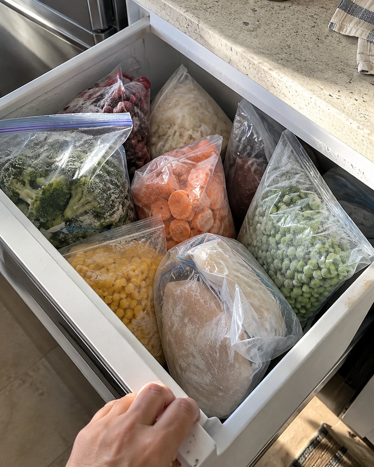 A freezer drawer pulled open to show upright bags of food with handwritten dates.