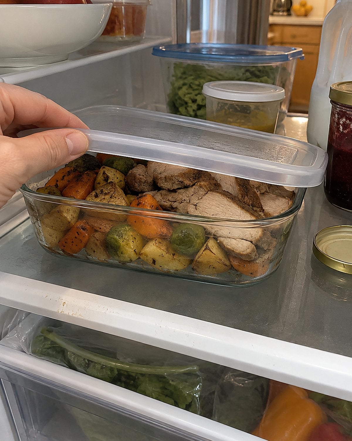 A shallow container of Sunday leftovers on a refrigerator shelf, with a handwritten date on the lid.