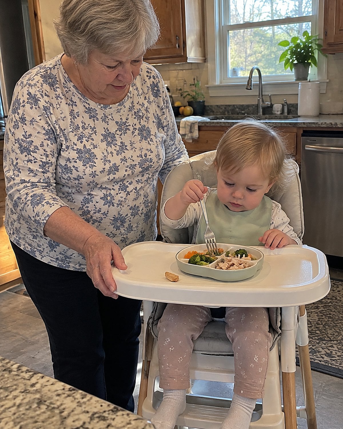 A grandchild in a high chair holding a fork above a partly eaten supper plate.