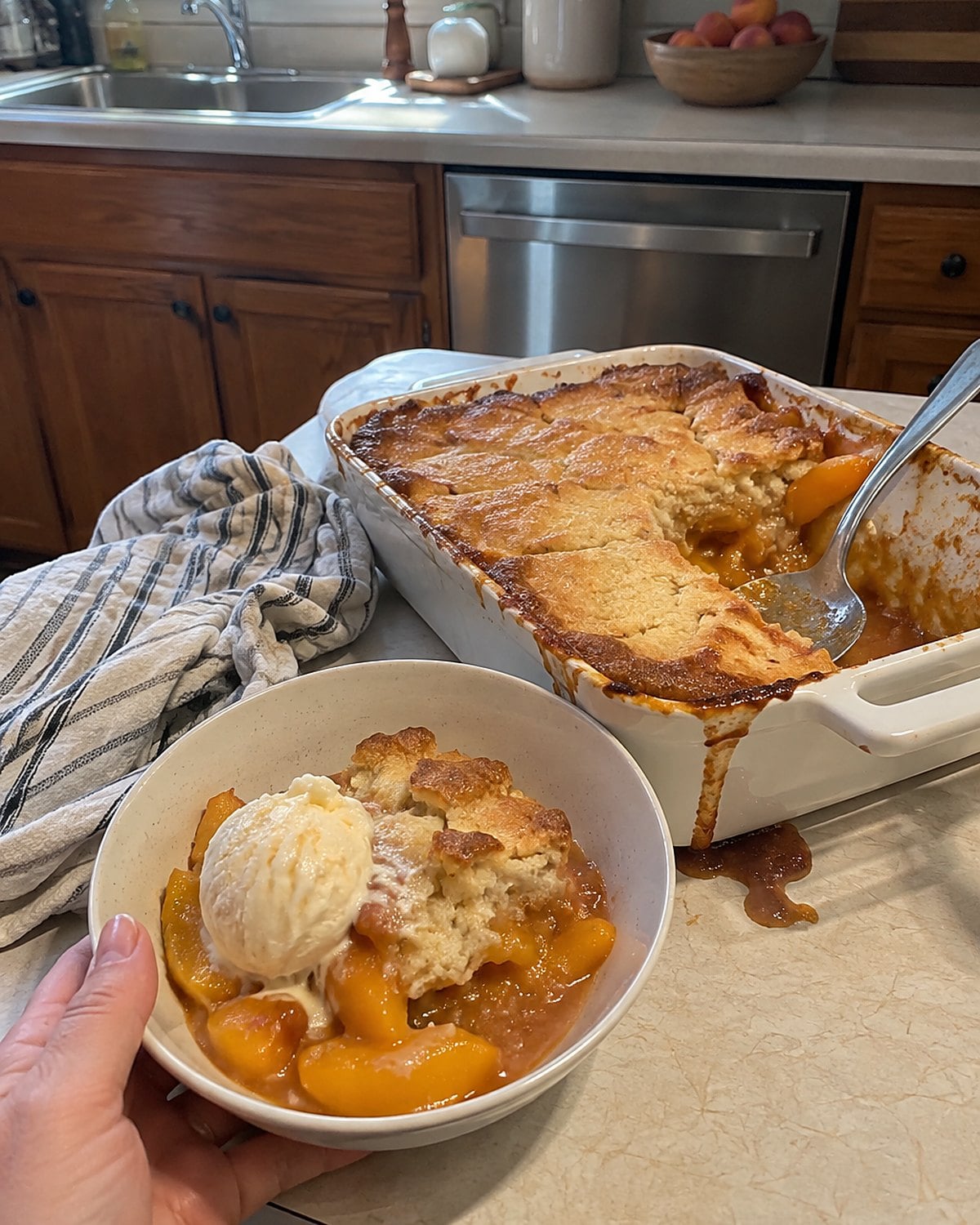 A small dish of peach cobbler on the counter, with fruit juice bubbled over one side.