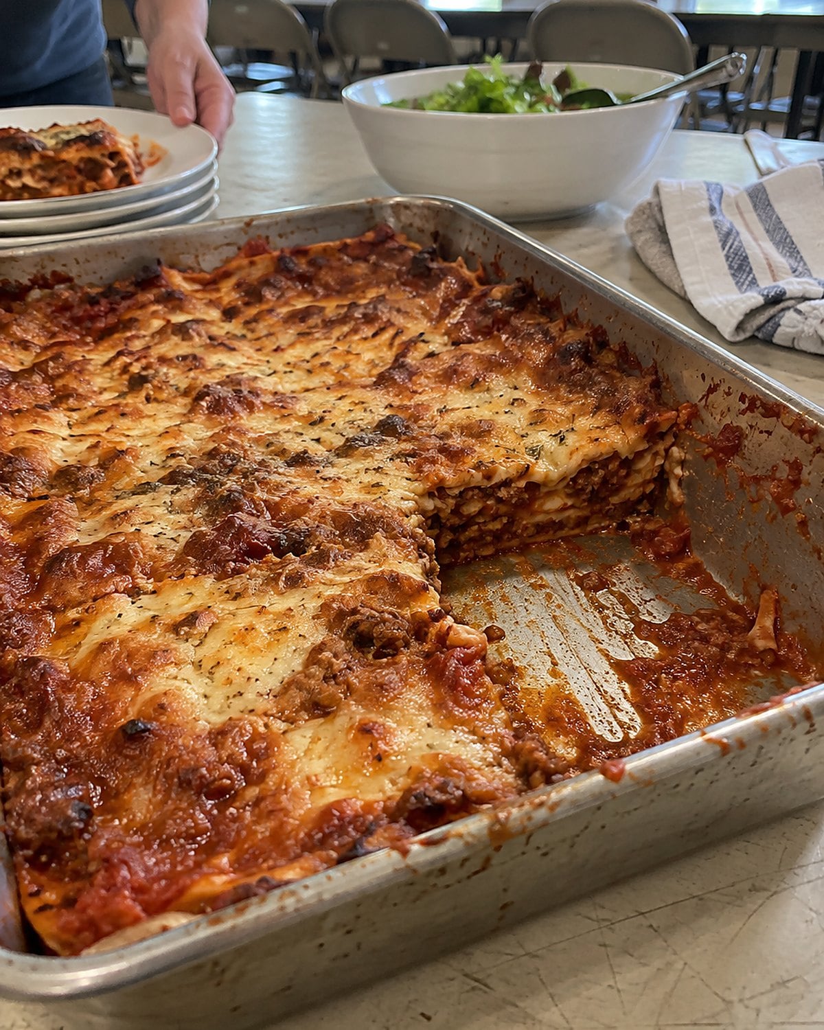 A scratched lasagna pan on a church hall table, with a corner serving missing.