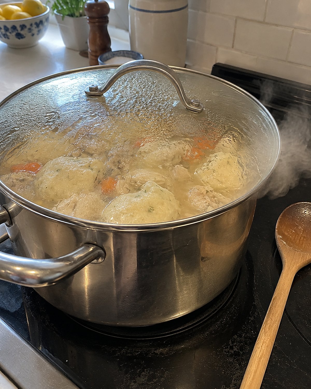 A lidded pot of chicken and dumplings on the stove, with steam escaping at one edge.