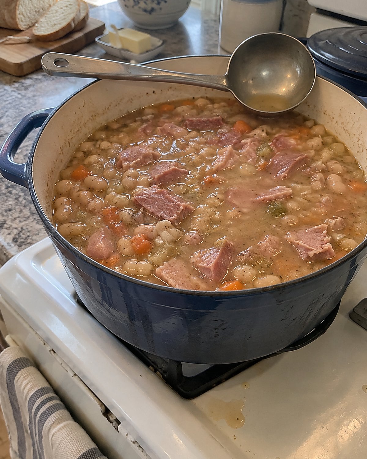 A soup pot of beans and ham on the stove, with a ladle resting across the rim.