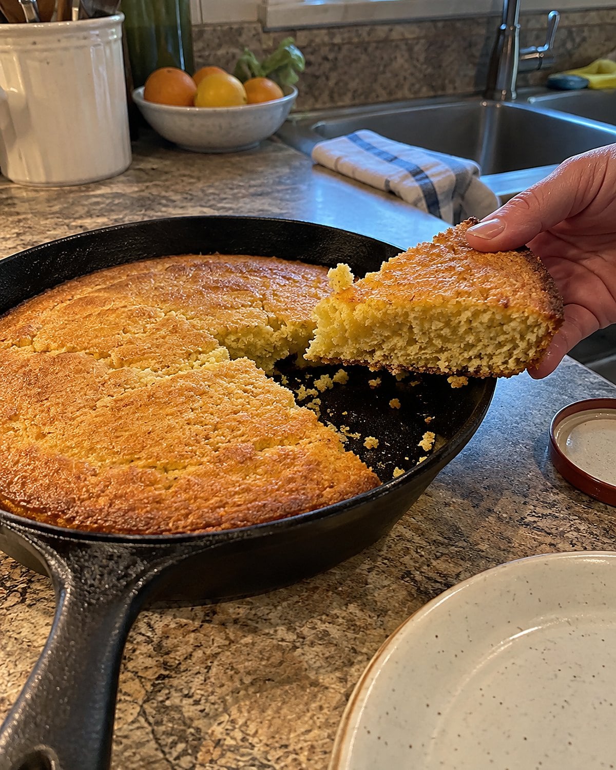 A cast-iron skillet of cornbread on the counter, with one uneven wedge lifted out.