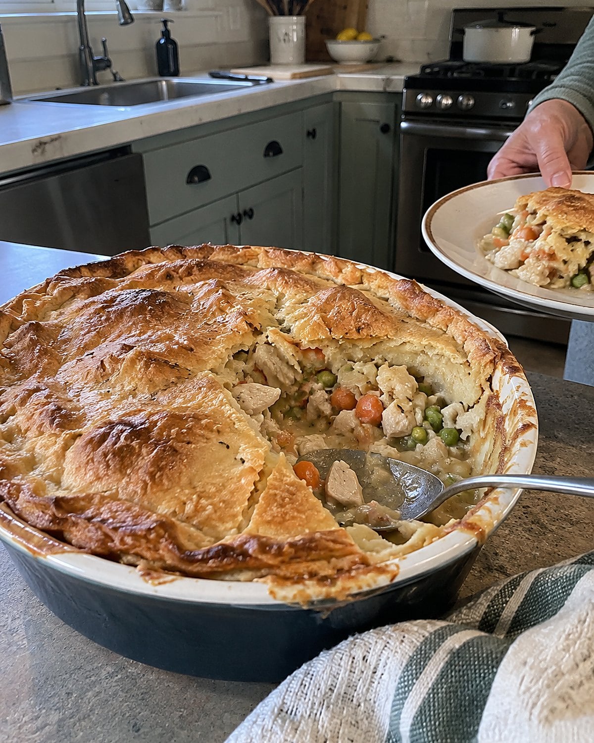 A chicken pot pie in a worn baking dish, its crust broken open by a serving spoon.