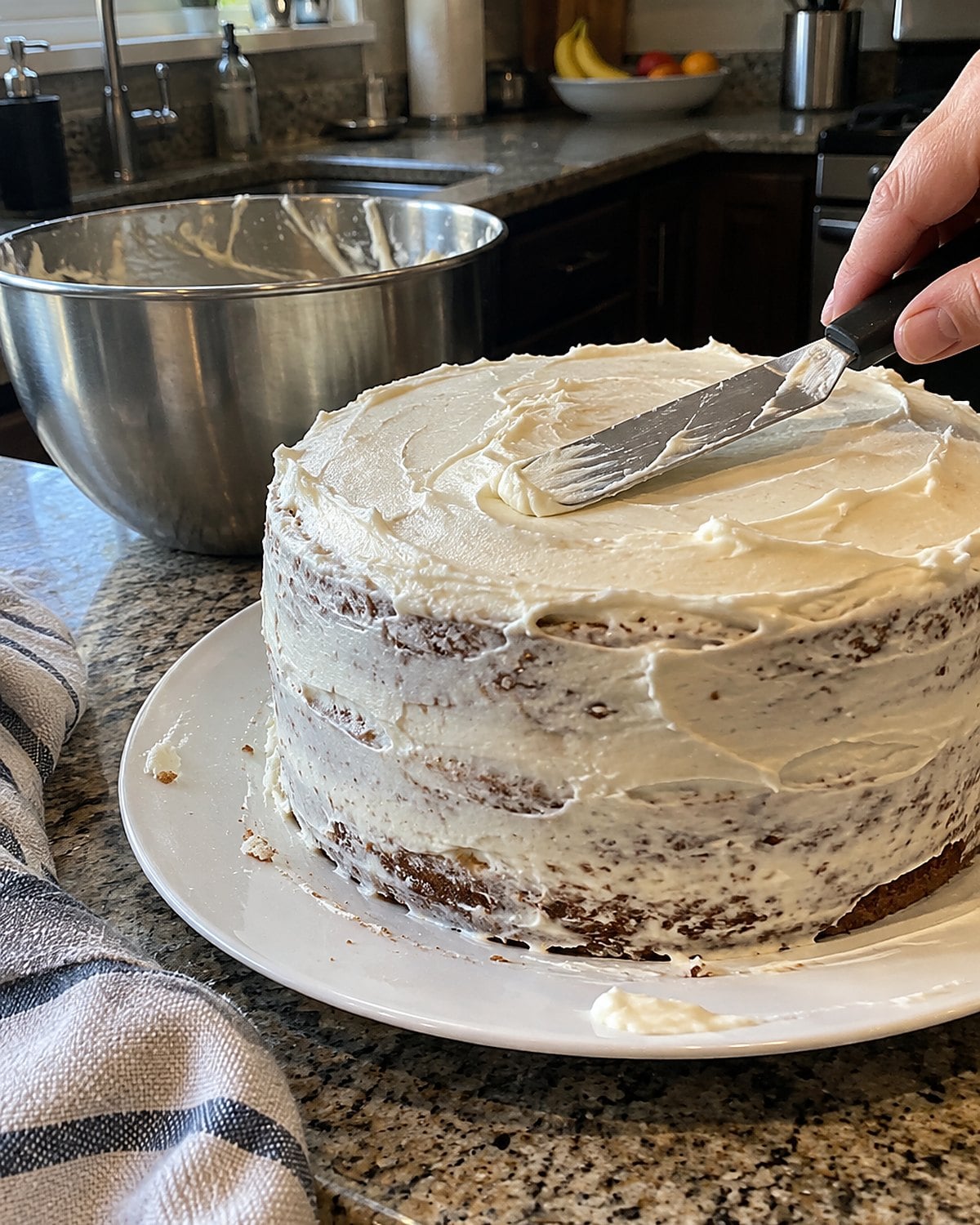 A partly frosted birthday cake on a kitchen counter, with crumbs caught in the first coat.