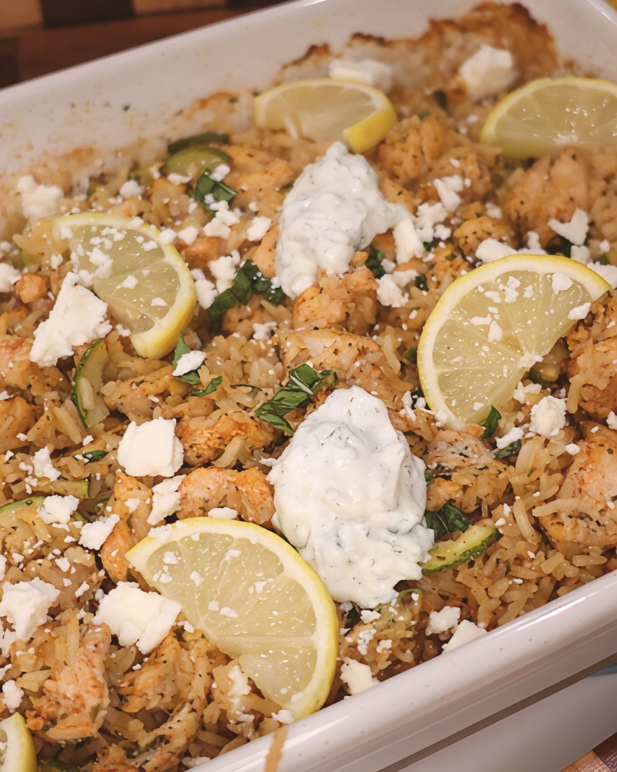 Dump and bake Greek chicken casserole topped with lemon slices, feta cheese, and tzatziki sauce.