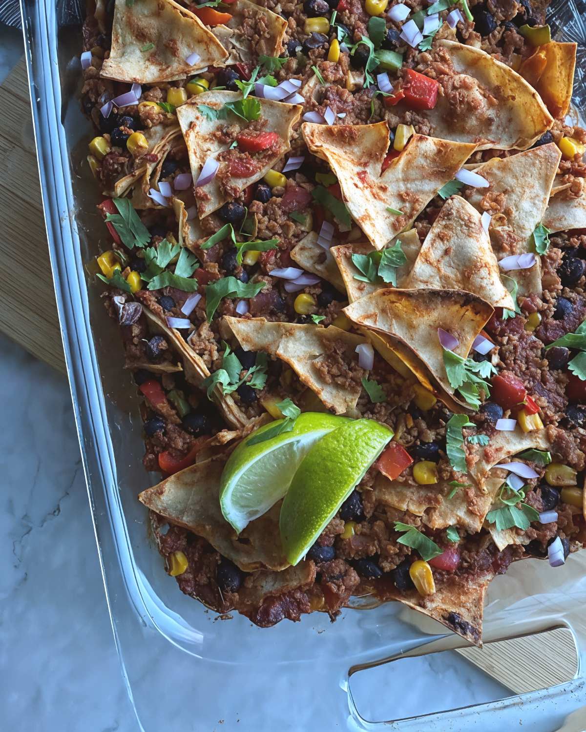 Vegan dump-and-bake taco casserole topped with tortilla chips, black beans, corn, and fresh lime slices.