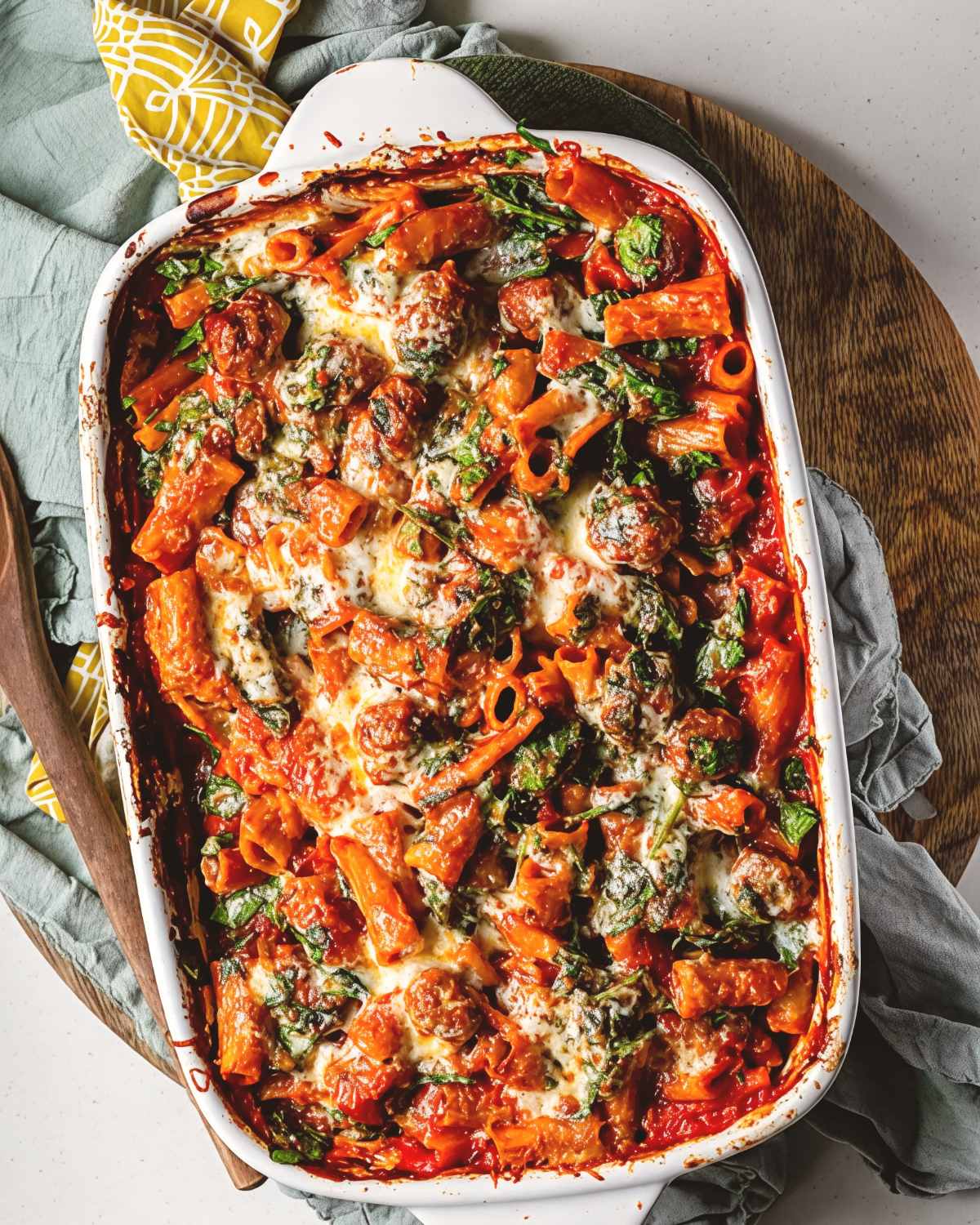 Easy sausage pasta dump and bake casserole in a white baking dish with melted cheese and spinach