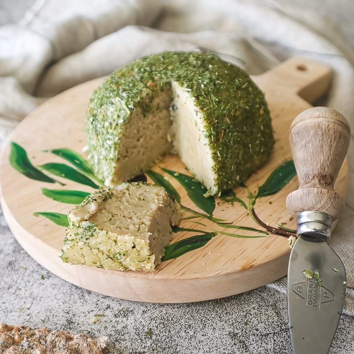An easy vegan truffle cheese ball coated in green herbs and sliced on a wooden board, served as one of the best vegan Thanksgiving appetizers.