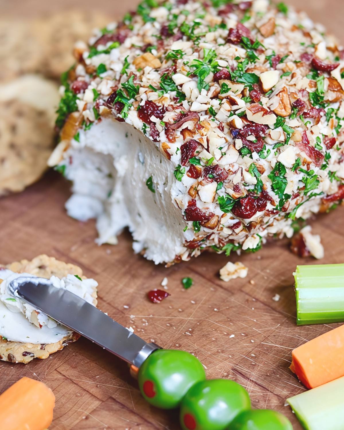 An easy vegan cheese ball coated with chopped pecans, cranberries, and fresh herbs, served on a board with crackers and vegetable sticks as one of the best vegan Thanksgiving appetizers