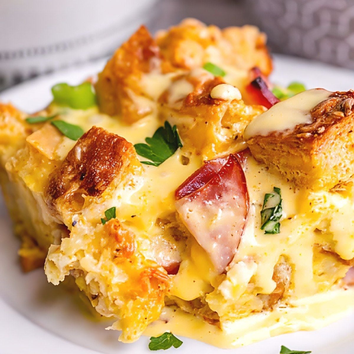 A serving of overnight eggs benedict casserole drizzled with creamy hollandaise sauce and fresh herbs on a plate as Thanksgiving breakfast ideas