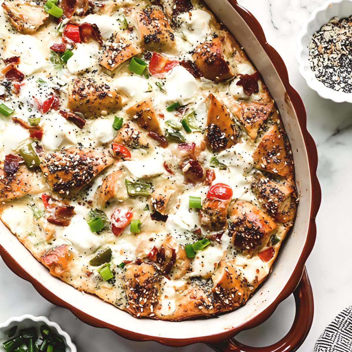 An everything bagel breakfast casserole baked in a dish and topped with cream cheese and seasonings as Thanksgiving breakfast ideas.