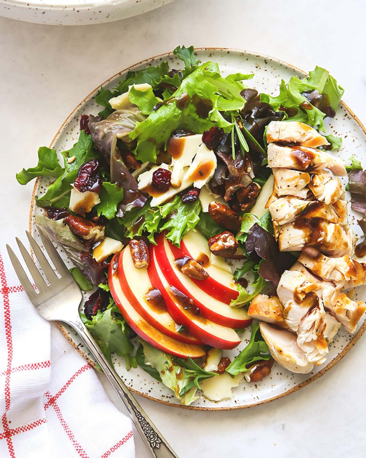 A vibrant plate of crisp leafy greens topped with sliced red apples, sharp cheddar, candied pecans, and dried cranberries drizzled with dressing, ideal for Thanksgiving side dishes for a crowd