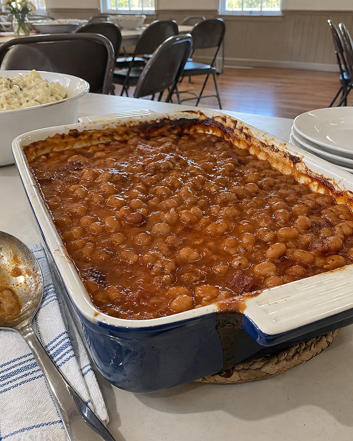 Baked beans bubble at the edge of a casserole dish on a church hall table.