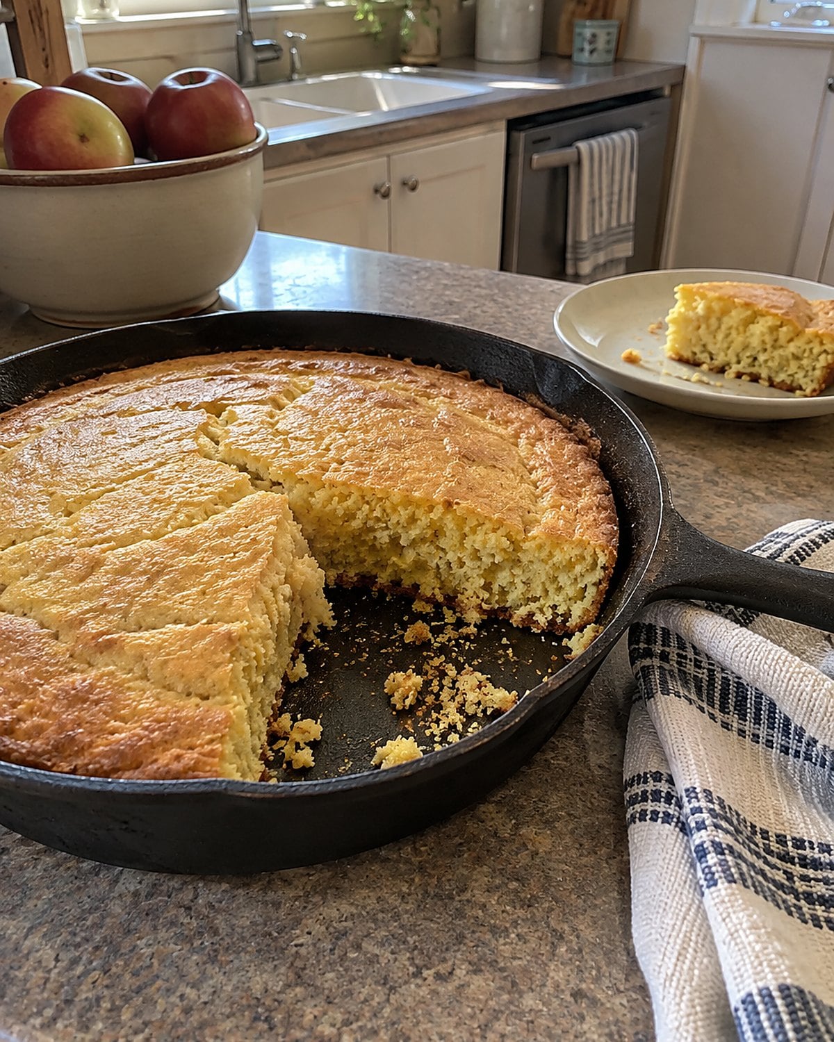 Cornbread with a missing corner sits in an iron skillet on a kitchen counter.