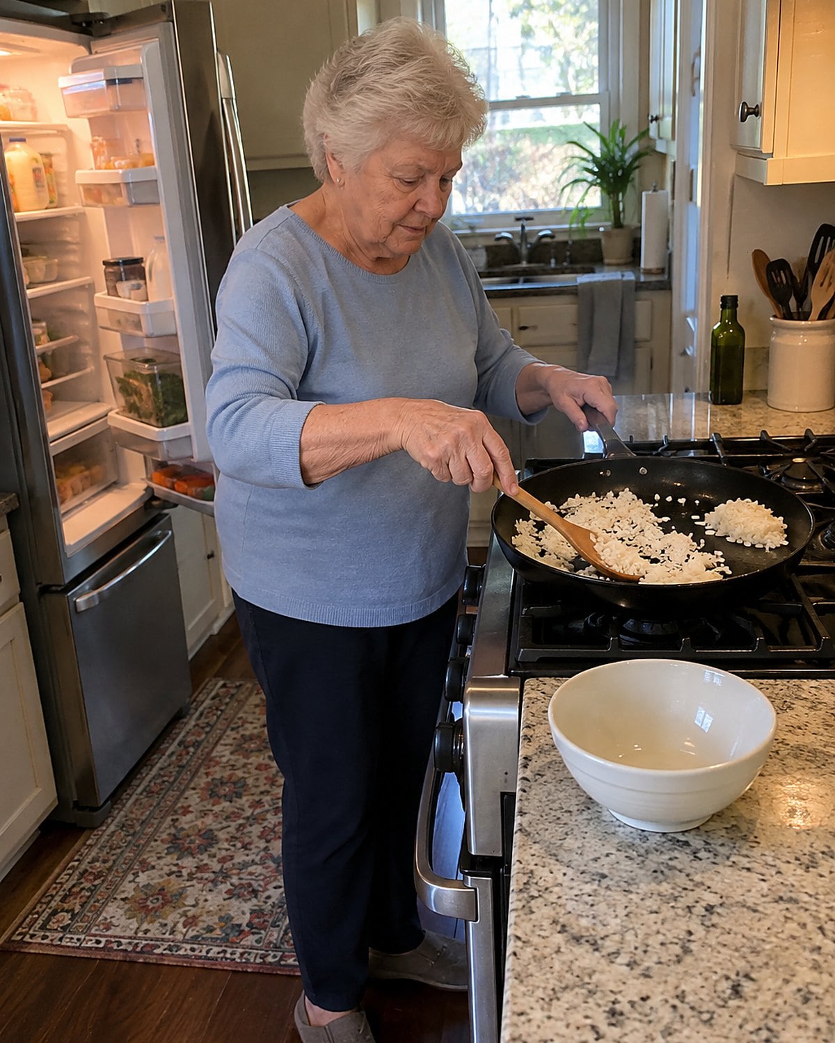 An older hand spreads cold rice across a hot skillet beside an open fridge.