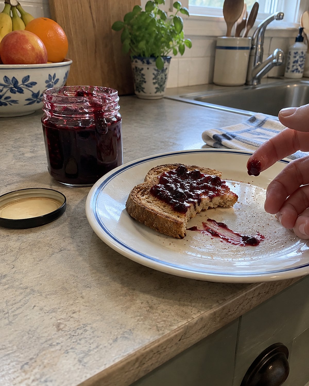 A small jar of berry jam beside a chilled plate marked by a fingertip.