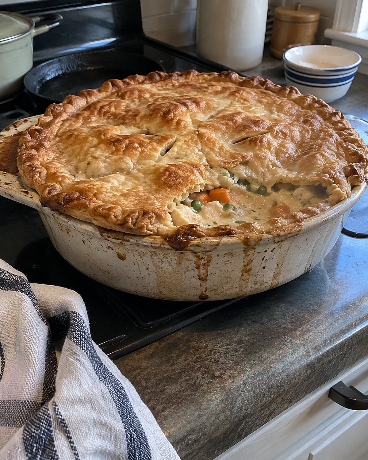 A chicken pot pie in a worn baking dish, with gravy bubbling through a gap in the crust.