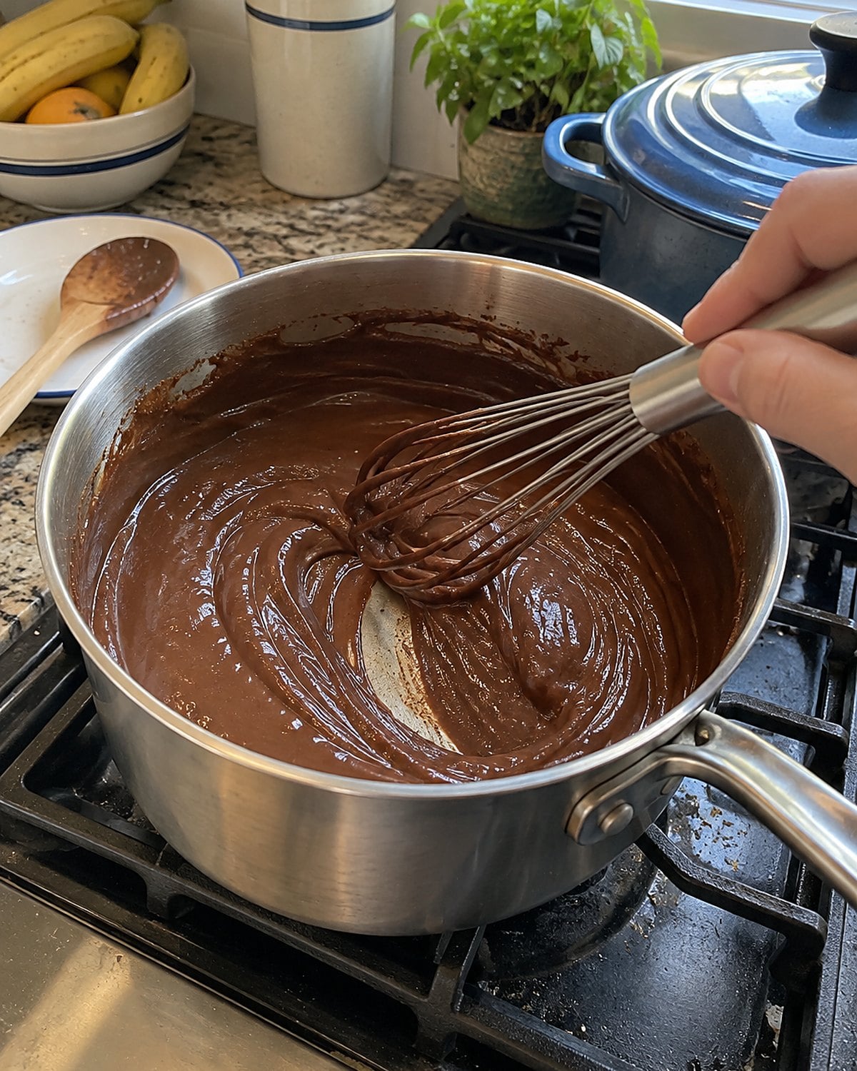 A whisk resting in a saucepan of chocolate pudding with a streak across the bottom.