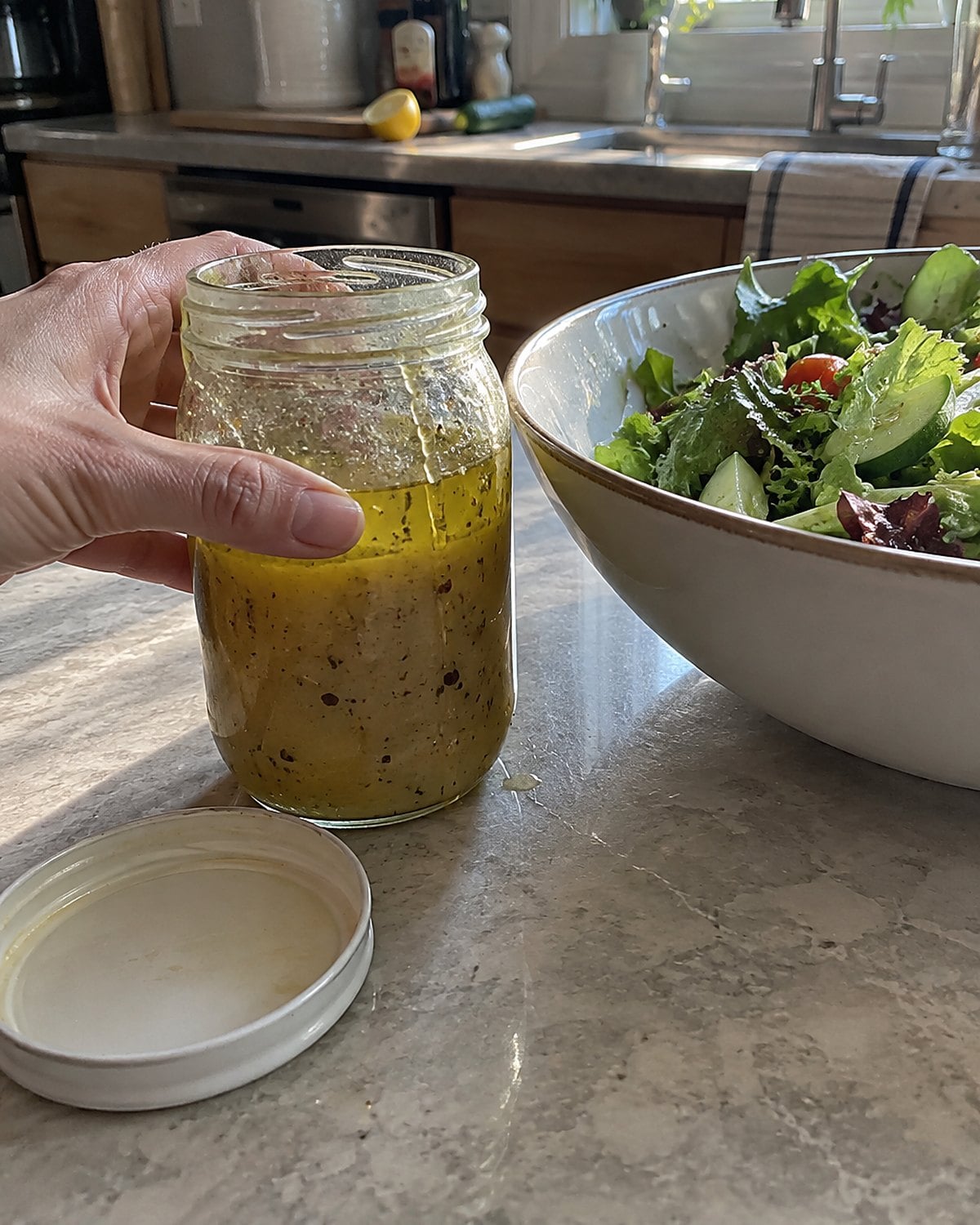 A small jar of dressing beside a bowl of greens, with oil separating at the top.