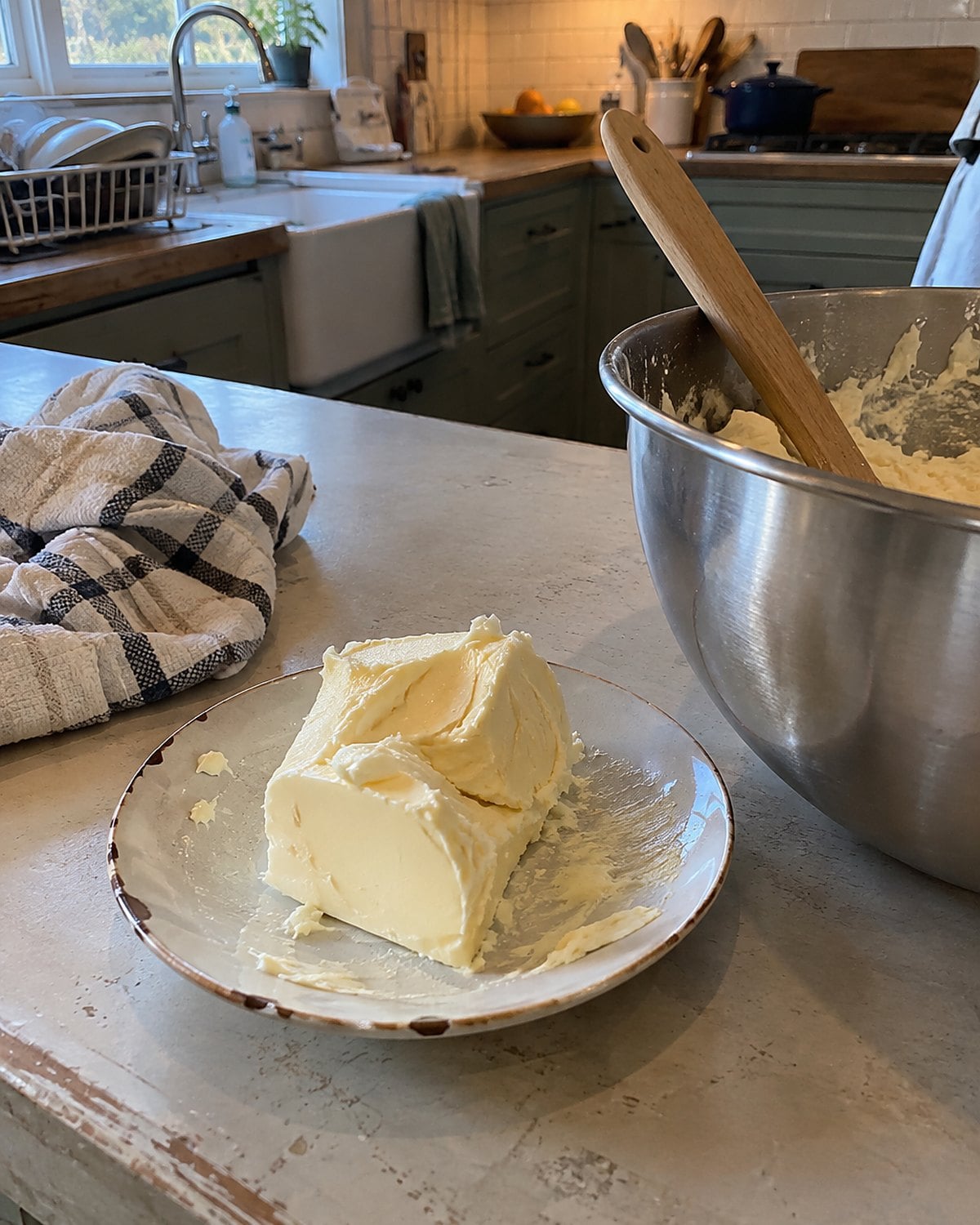 A small mound of fresh butter on a chipped saucer beside a mixer bowl.