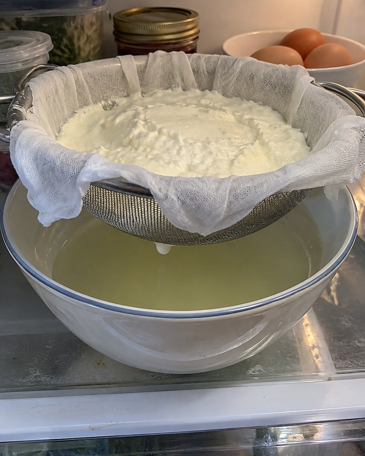 A cloth-lined strainer of thick yogurt over a deep bowl in the refrigerator.