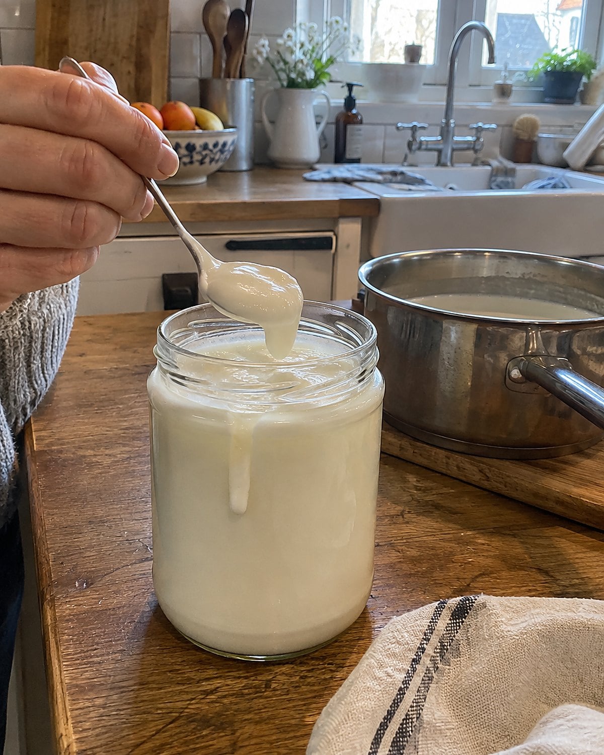 A warm yogurt jar beside a milk pot on a home kitchen counter.