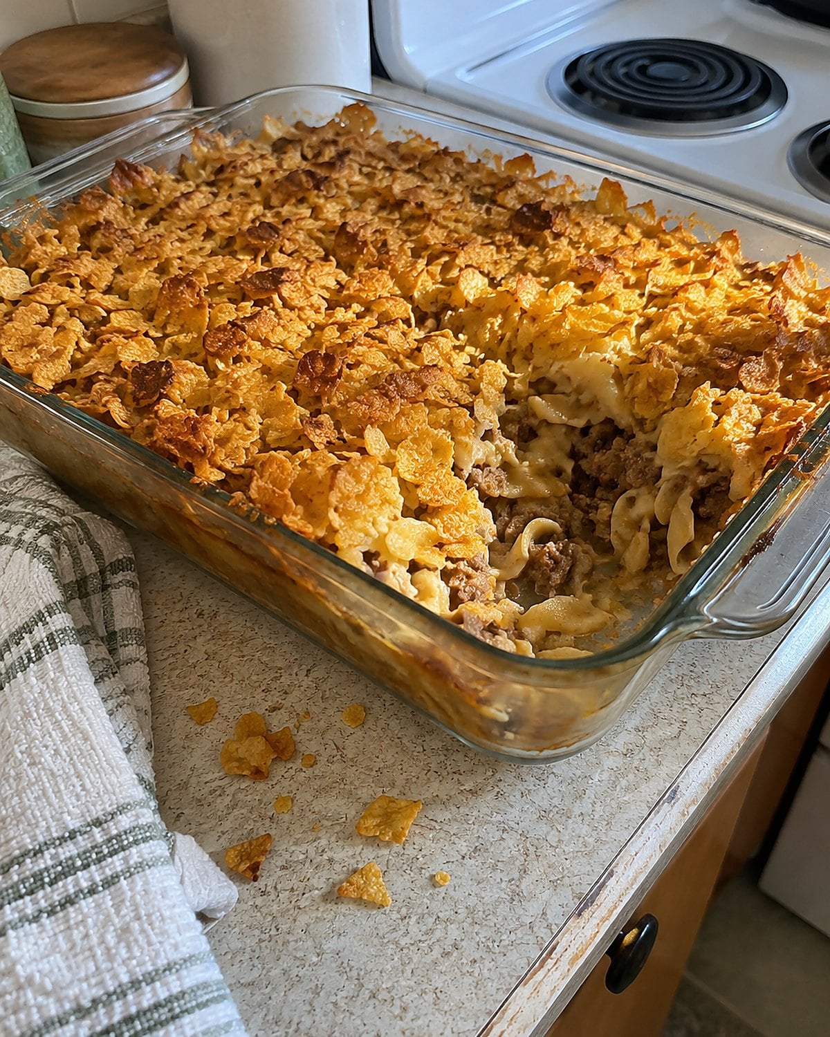 Crushed cornflakes scattered across a hamburger noodle bake in a glass dish.