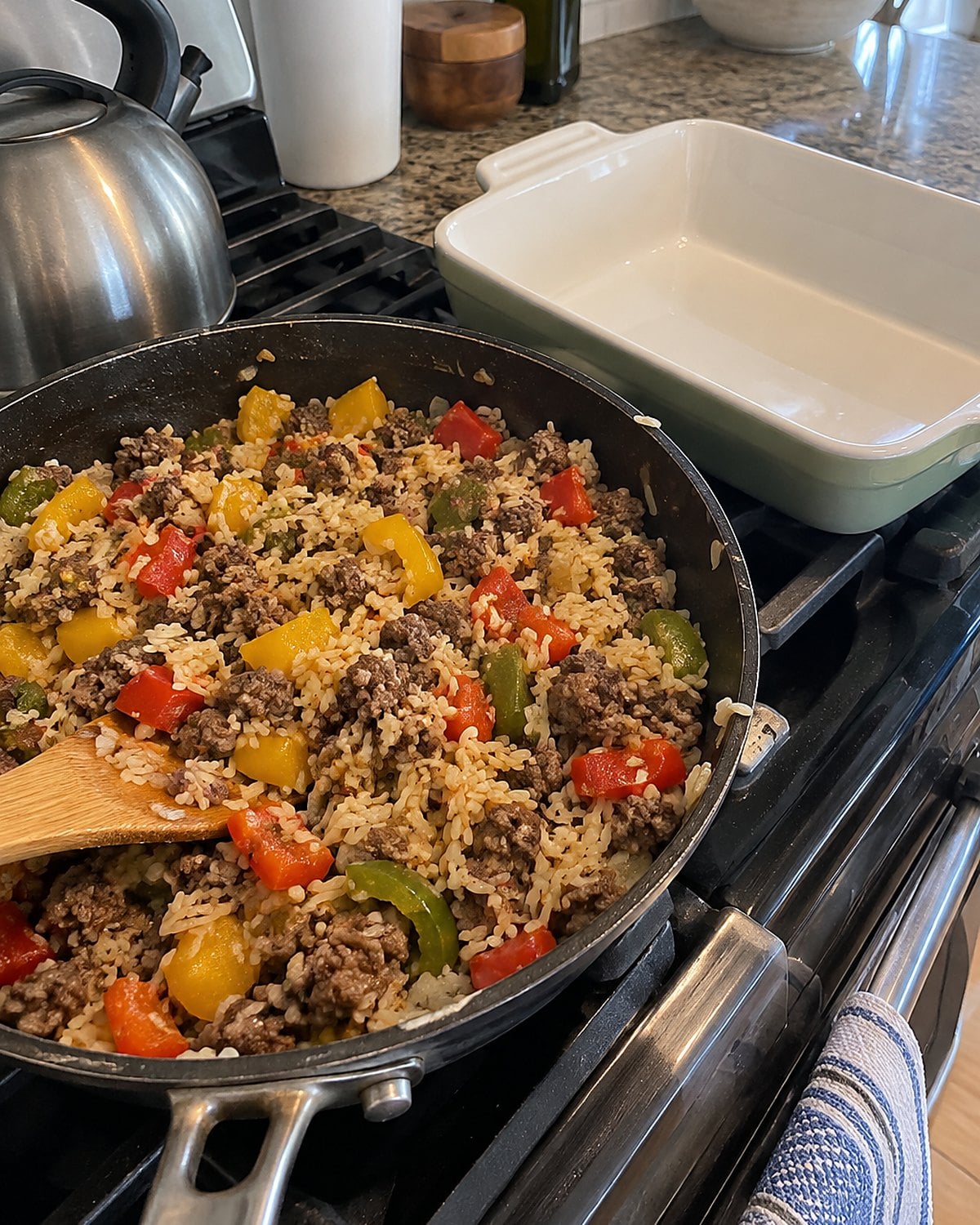 A skillet of chopped peppers, beef, and rice beside an empty casserole dish on the stove.