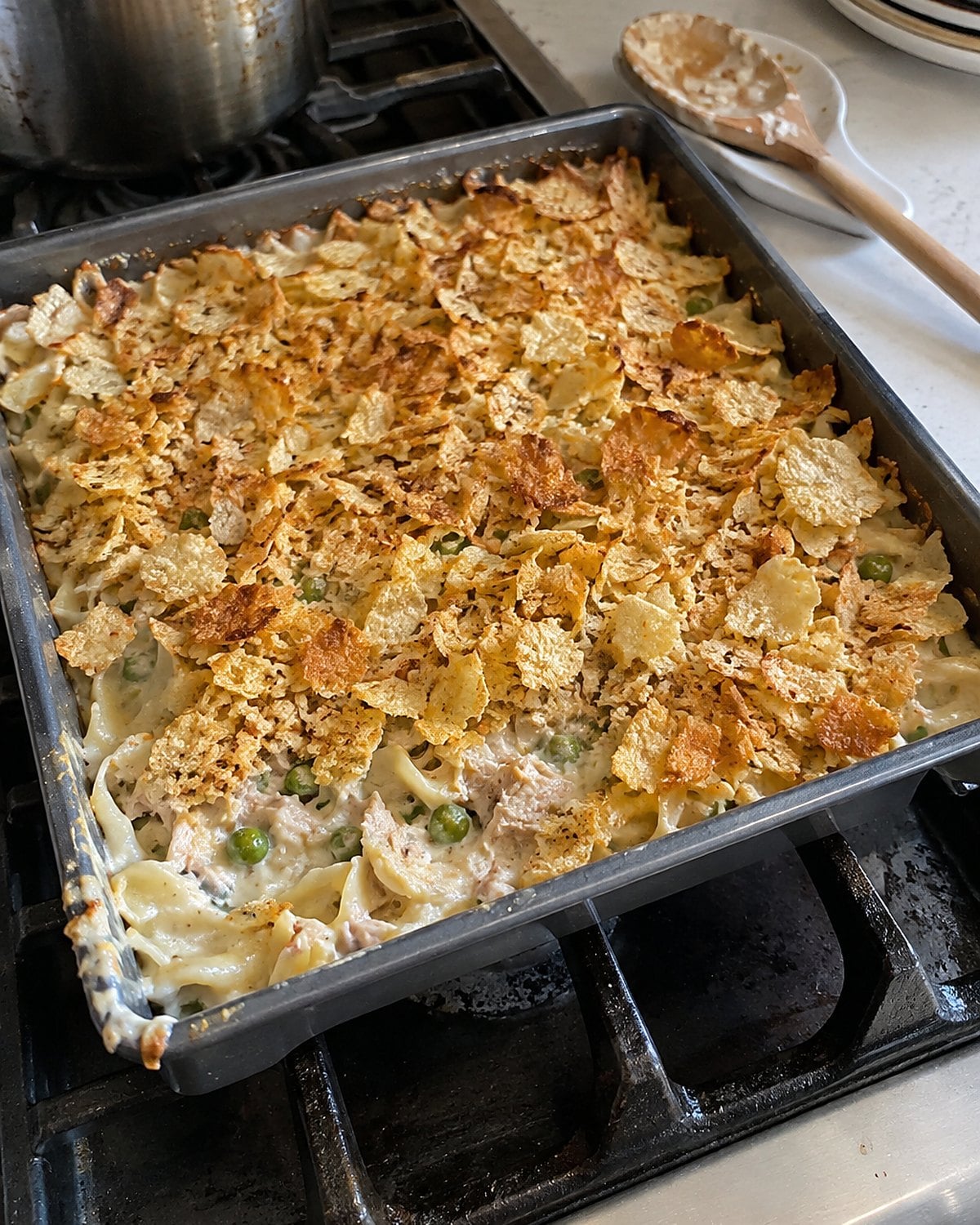 A slightly uneven tuna noodle casserole in a square pan on the stove, with crushed potato chips browned across the top.