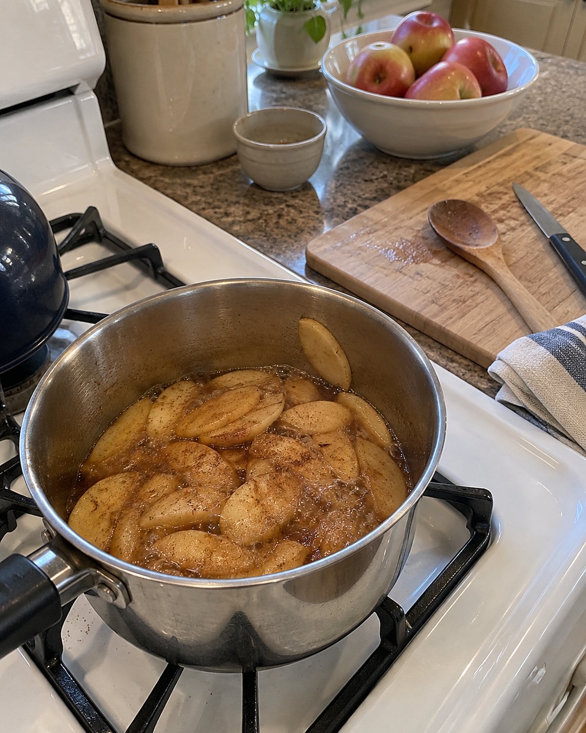 Cinnamon apple slices in a small saucepan on a white stove, with a knife on the counter.