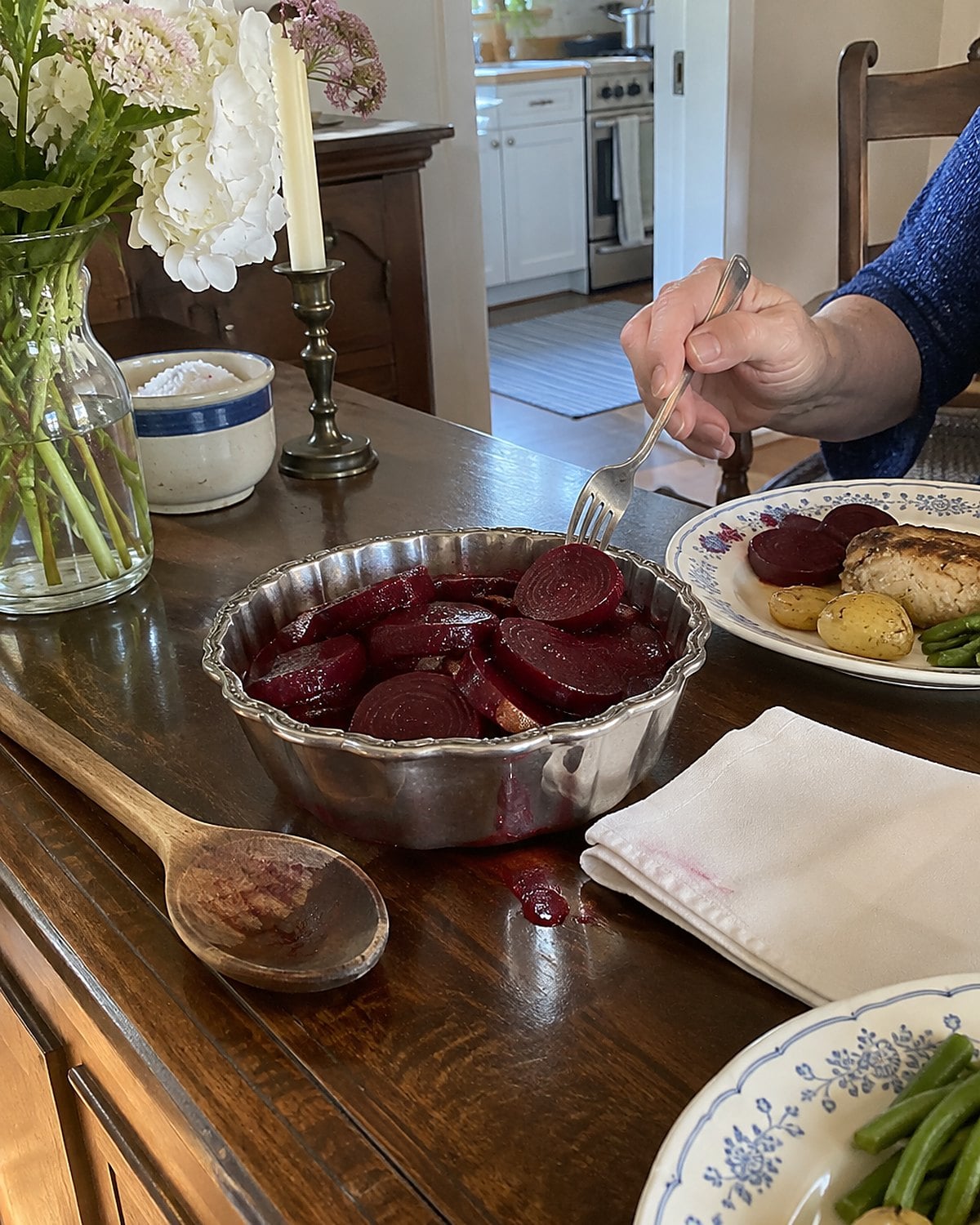Pickled beets in a small silver dish beside a folded white napkin on the dining room sideboard.