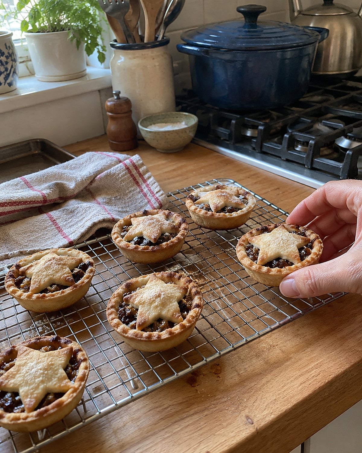 Small mince pies cooling on a rack beside the stove, one with a crooked pastry star.