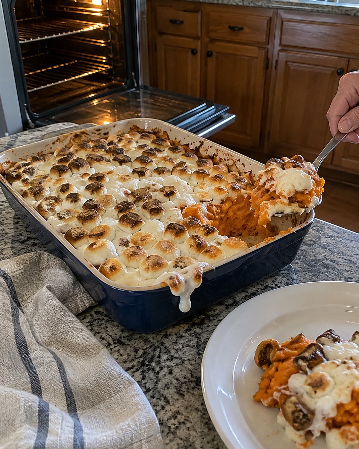 A pan of sweet potatoes with unevenly browned marshmallows resting beside the oven.