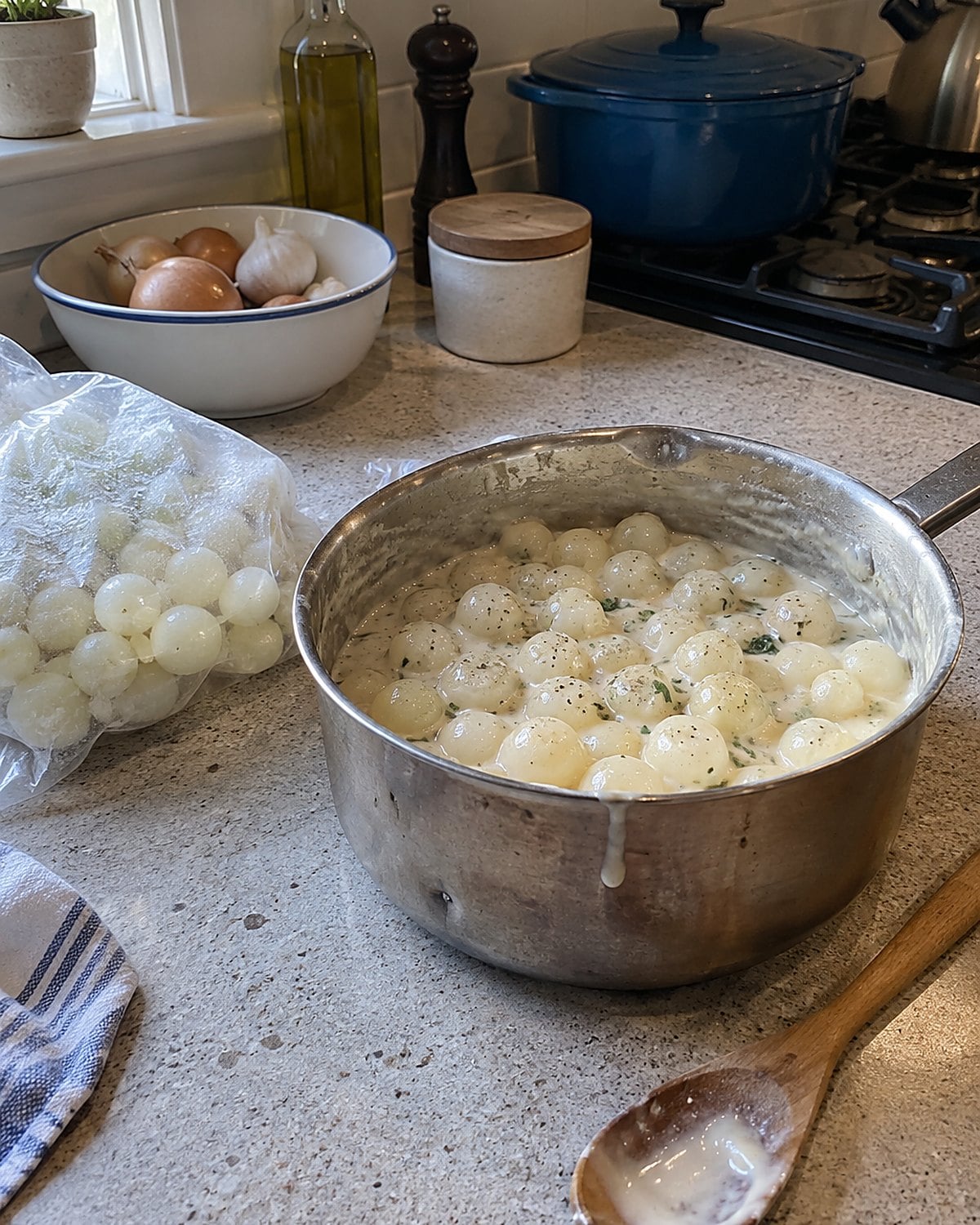 Pearl onions coated in white sauce in a saucepan beside a bag of frozen onions.