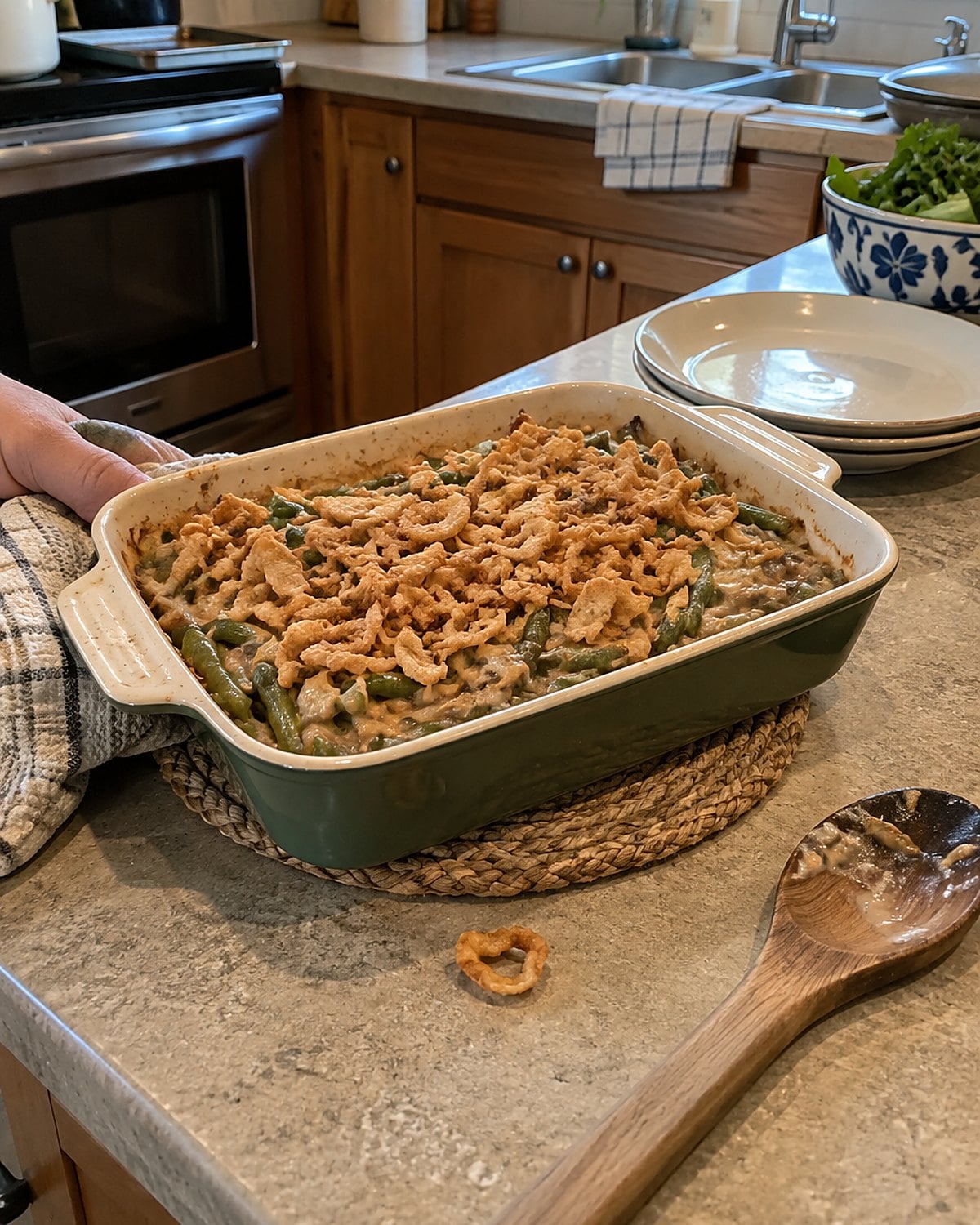 Green bean casserole with scattered crisp onions in a small baking dish on a trivet.
