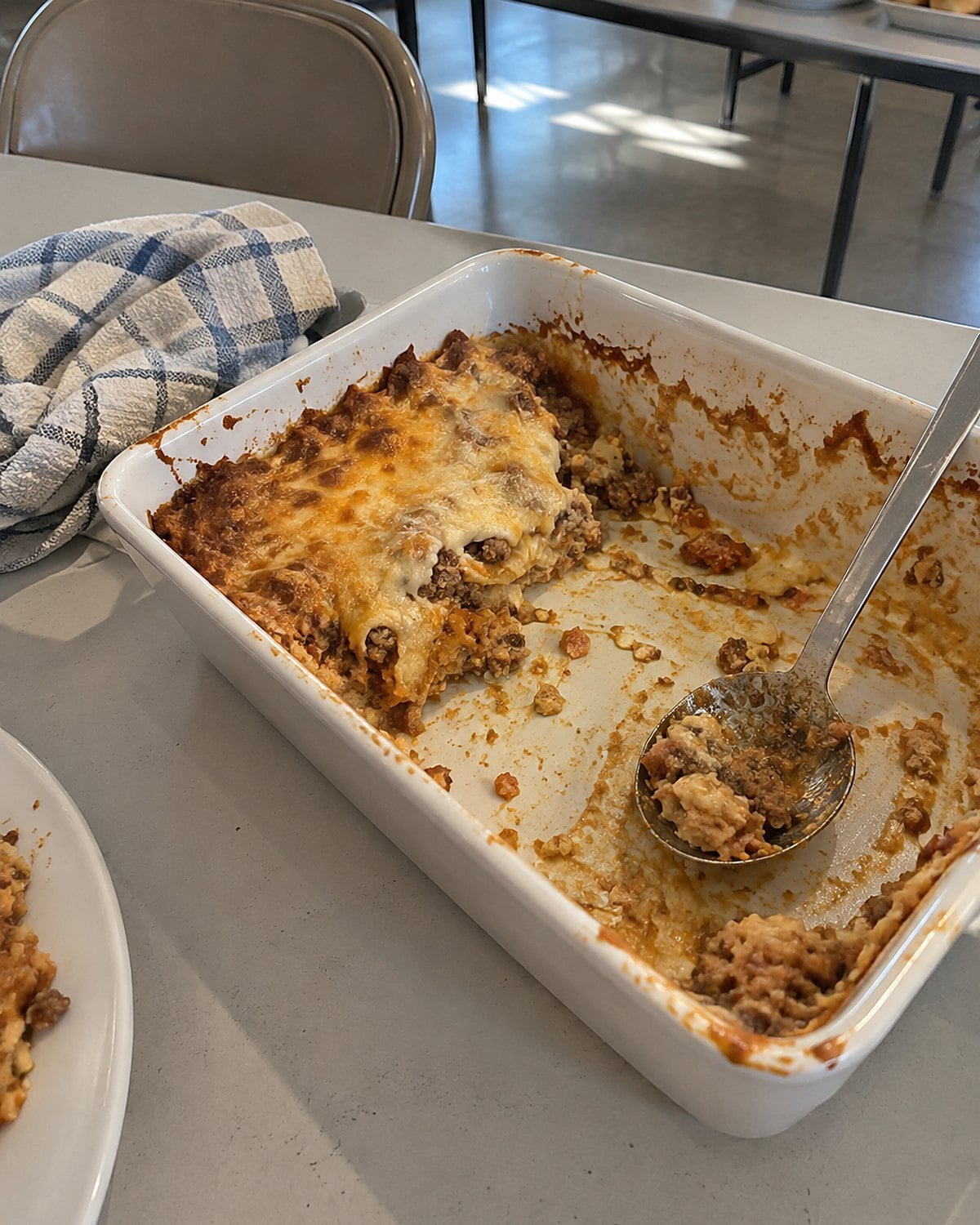 A serving spoon resting in an almost empty casserole dish on a church hall table.