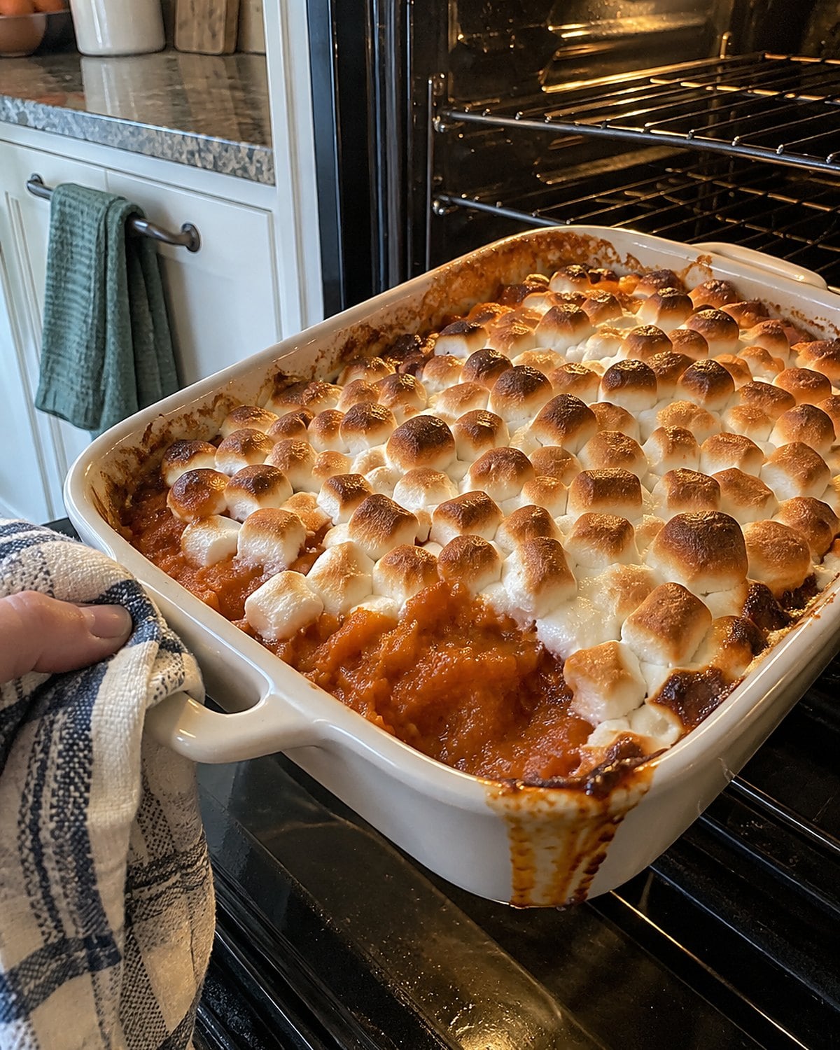 A baking dish of sweet potatoes with patchily browned marshmallows on the oven door.