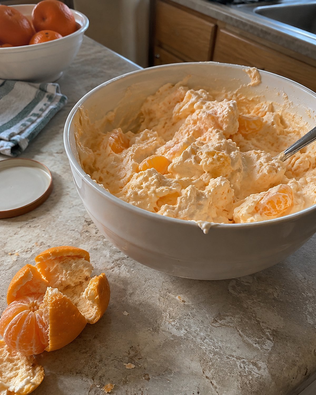 A bowl of orange fluff beside a half-peeled mandarin on a kitchen counter.