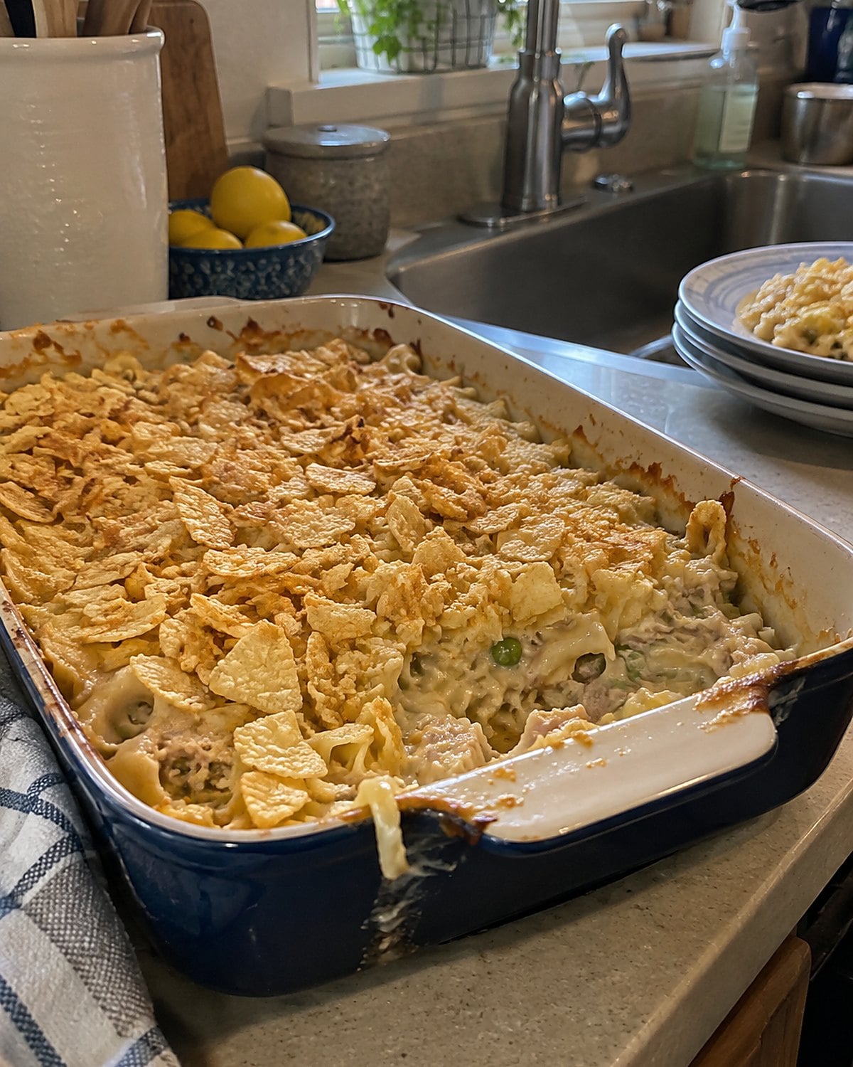 A pan of tuna noodle casserole near the sink, with crushed chips scattered across its uneven top.